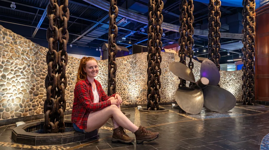 A woman beside the anchor chains and ship propeller