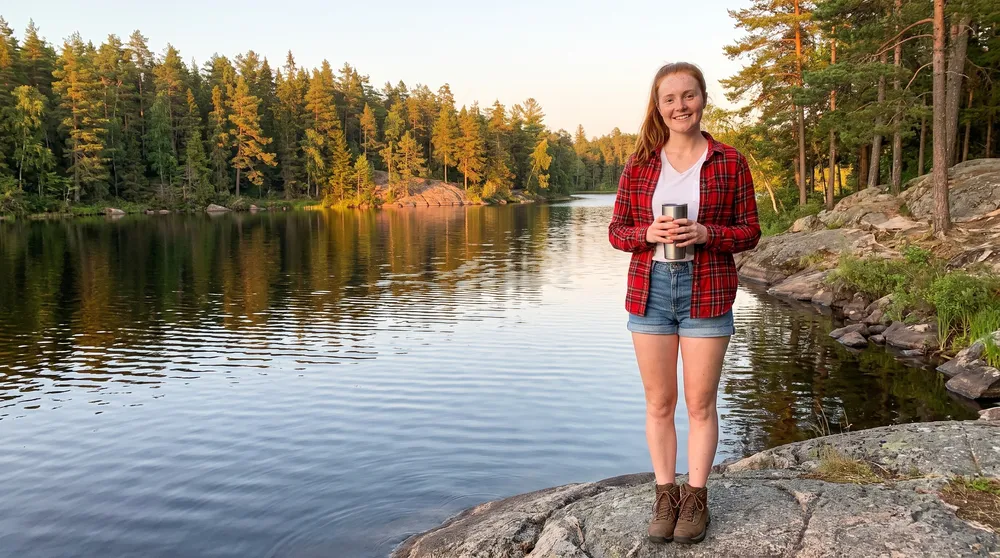 A woman by a calm lake with a travel mug